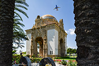 Exterior of a gilded shrine with aircraft overhead and flowers in the foreground